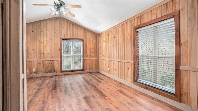 spare room featuring ceiling fan, a textured ceiling, wooden walls, wood finished floors, and vaulted ceiling