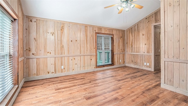 spare room with baseboards, a ceiling fan, lofted ceiling, wood finished floors, and wood walls