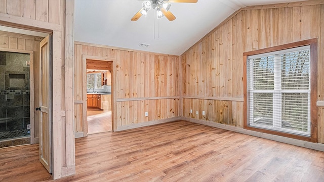 unfurnished room with lofted ceiling, visible vents, ceiling fan, wooden walls, and wood finished floors