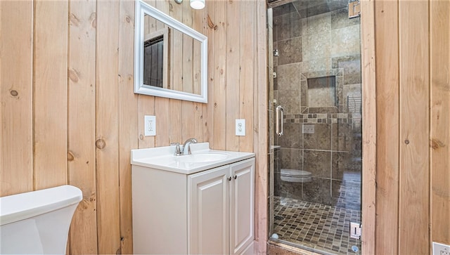 full bathroom featuring wood walls, a stall shower, vanity, and toilet