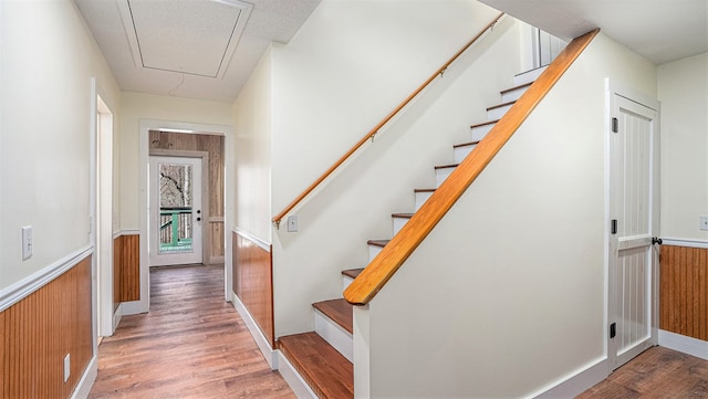 stairs with wood walls, attic access, wood finished floors, and wainscoting