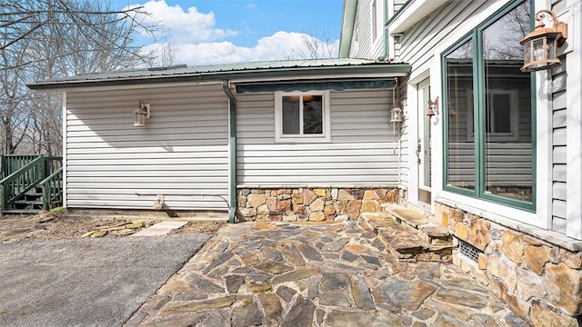 view of side of home featuring stone siding, a patio area, and metal roof