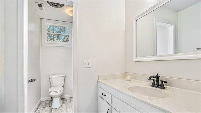 bathroom with toilet, wood finished floors, vanity, visible vents, and baseboards