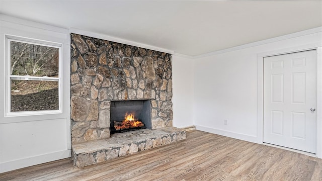 unfurnished living room with crown molding, a stone fireplace, baseboards, and wood finished floors