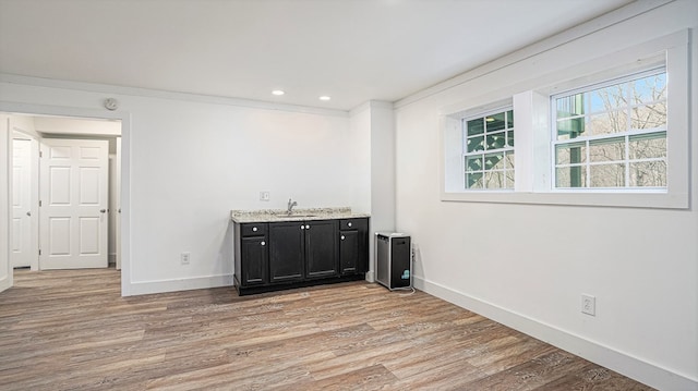 bar featuring light wood finished floors, baseboards, a sink, and recessed lighting