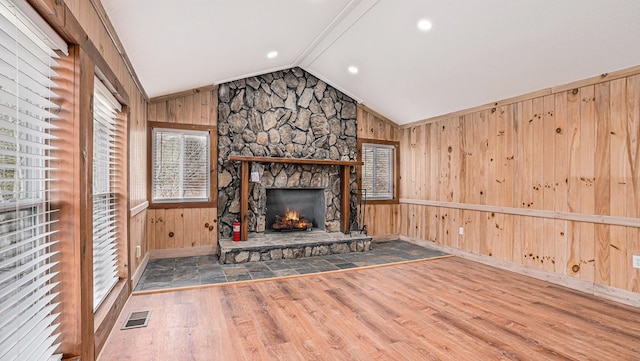 unfurnished living room with lofted ceiling, wooden walls, visible vents, and wood finished floors