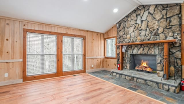 unfurnished living room with lofted ceiling, wooden walls, a fireplace, and wood finished floors