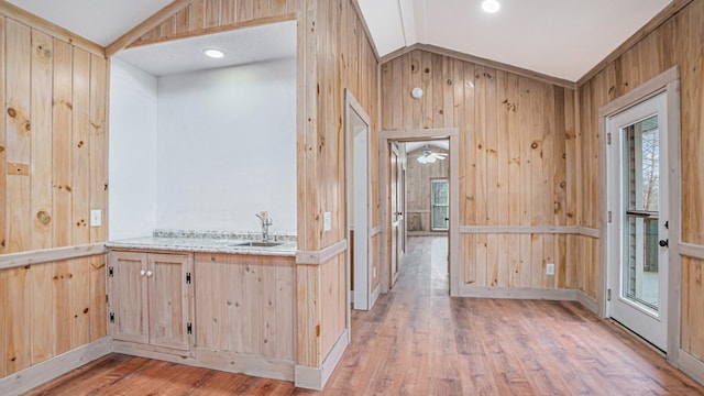 kitchen with light brown cabinets, light wood-style flooring, wooden walls, a healthy amount of sunlight, and vaulted ceiling