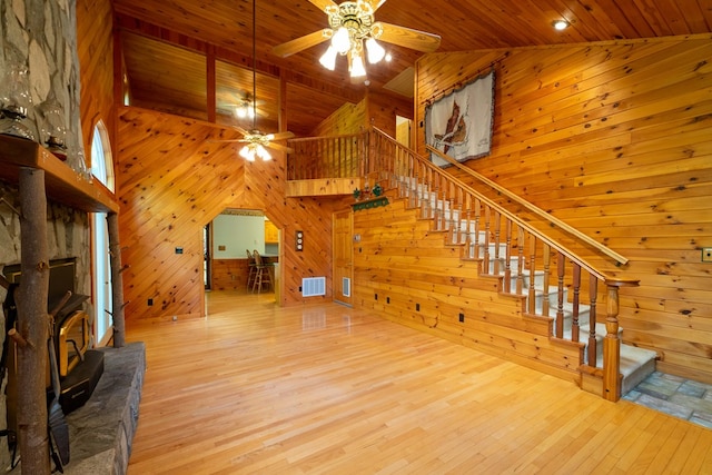 unfurnished living room featuring a wood stove, ceiling fan, a high ceiling, light hardwood / wood-style floors, and wood ceiling