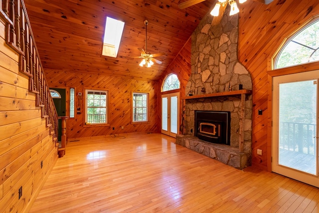 unfurnished living room with a skylight, ceiling fan, high vaulted ceiling, and a wood stove