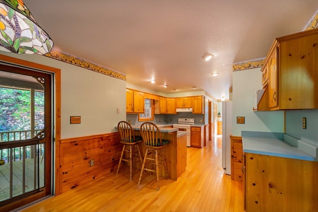 kitchen featuring light hardwood / wood-style floors, a textured ceiling, white appliances, wooden walls, and a breakfast bar