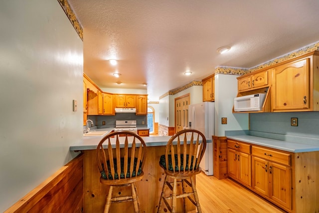 kitchen with a textured ceiling, white appliances, sink, light hardwood / wood-style flooring, and a breakfast bar area