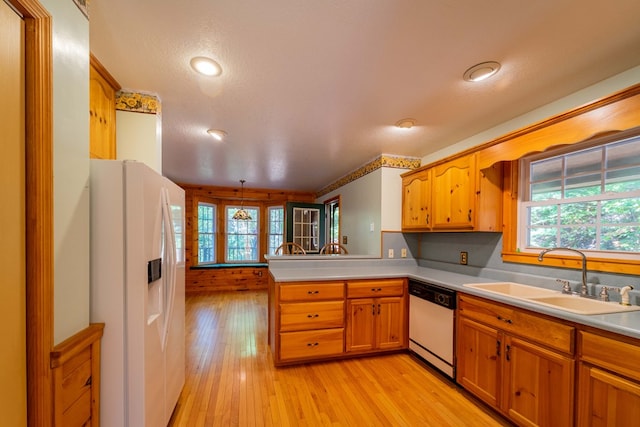 kitchen featuring kitchen peninsula, light wood-type flooring, white appliances, sink, and pendant lighting