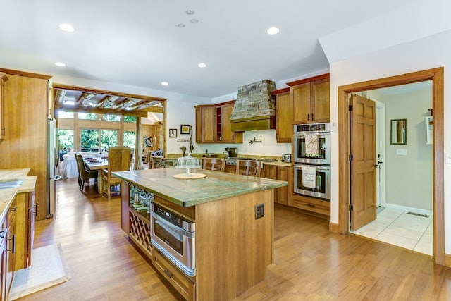 kitchen featuring appliances with stainless steel finishes, light hardwood / wood-style flooring, custom range hood, and a kitchen island