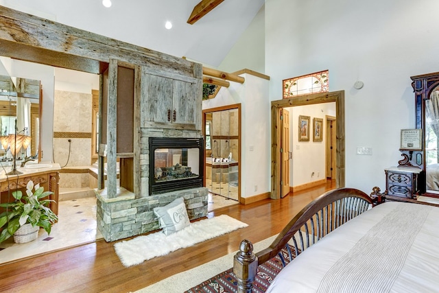 bedroom featuring light hardwood / wood-style floors, a stone fireplace, and high vaulted ceiling