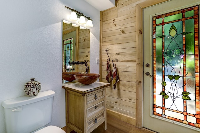 bathroom featuring vanity, toilet, wood-type flooring, and wooden walls