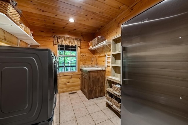 clothes washing area featuring wood walls, wooden ceiling, sink, light tile patterned floors, and washer / clothes dryer