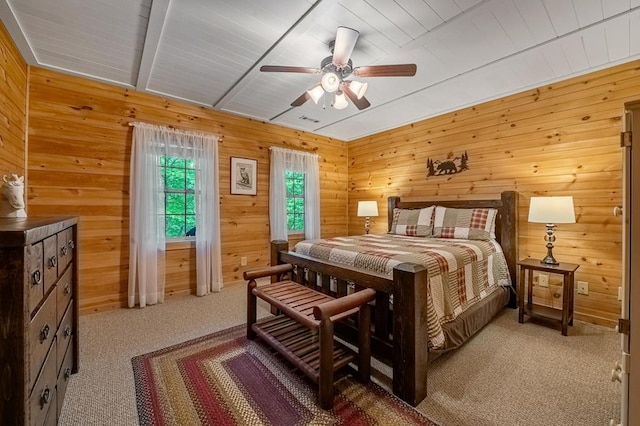 bedroom with ceiling fan, beamed ceiling, light colored carpet, and wood walls