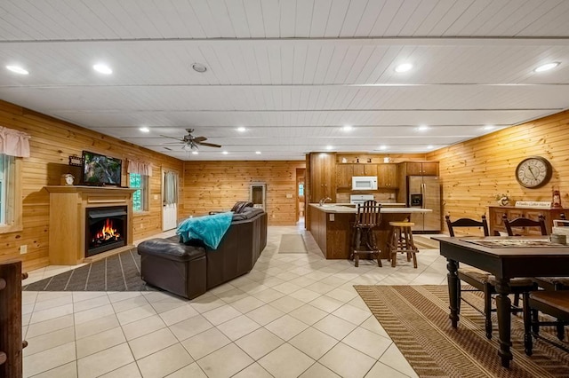 living room featuring wooden walls, ceiling fan, and light tile patterned floors