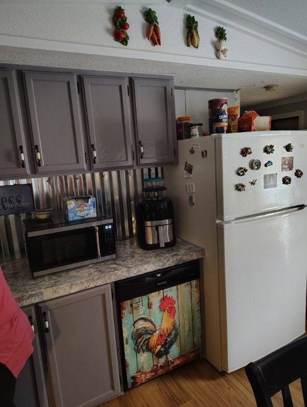 kitchen with stainless steel microwave, gray cabinetry, dishwasher, light countertops, and freestanding refrigerator