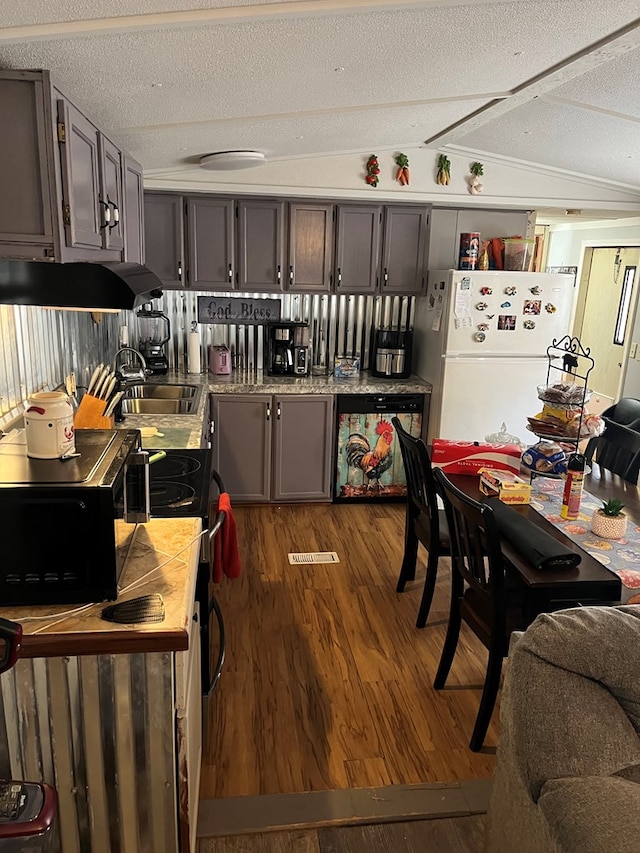 kitchen with dark wood-type flooring, a sink, under cabinet range hood, freestanding refrigerator, and vaulted ceiling