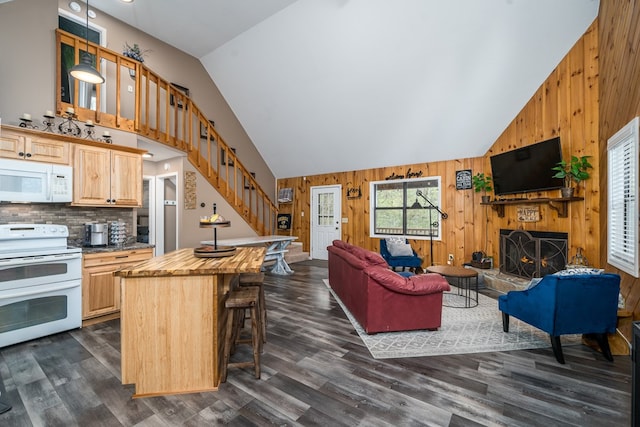living area with a large fireplace, dark wood-style flooring, high vaulted ceiling, stairs, and wood walls