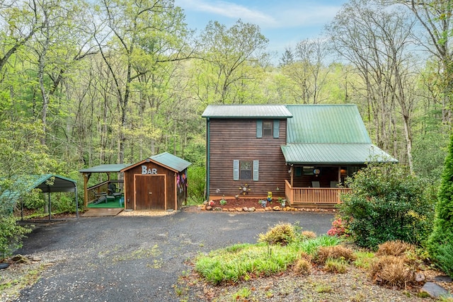 chalet / cabin featuring a porch, metal roof, a carport, a view of trees, and a storage unit
