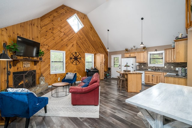 living room featuring wooden walls, dark wood-style floors, high vaulted ceiling, and a warm lit fireplace