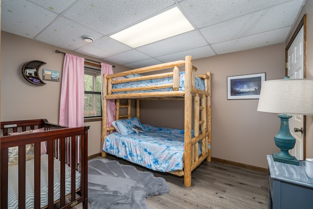 bedroom with a paneled ceiling, wood finished floors, and baseboards