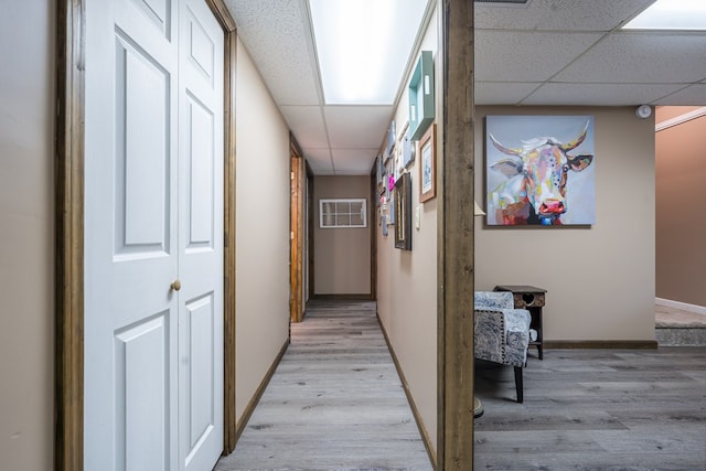 hall featuring a paneled ceiling, baseboards, and light wood-type flooring
