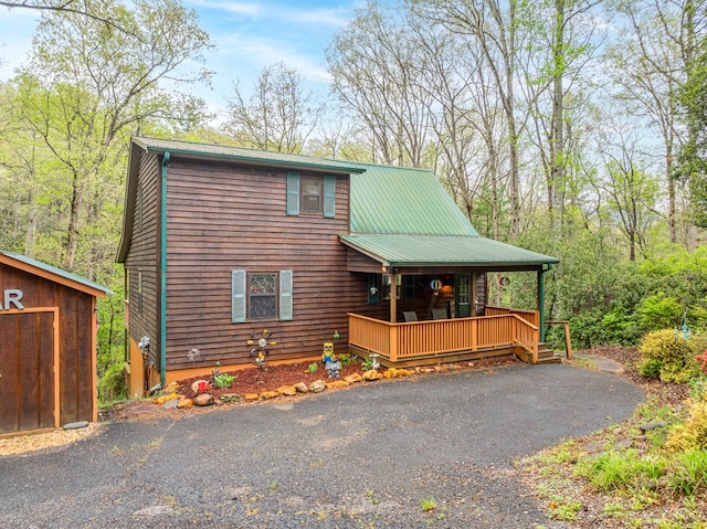 rustic home with covered porch, metal roof, aphalt driveway, and an outbuilding