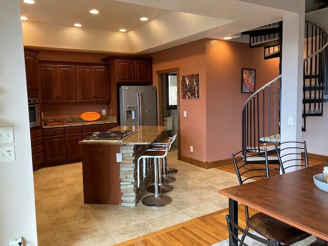 kitchen with light stone countertops, a kitchen breakfast bar, stainless steel appliances, light tile floors, and a center island