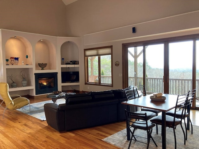 living room with a towering ceiling, built in features, and light wood-type flooring