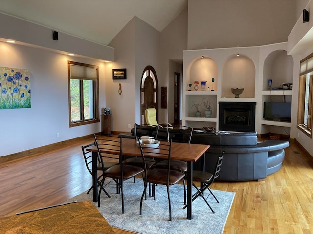 dining area featuring high vaulted ceiling, light hardwood / wood-style floors, and built in shelves