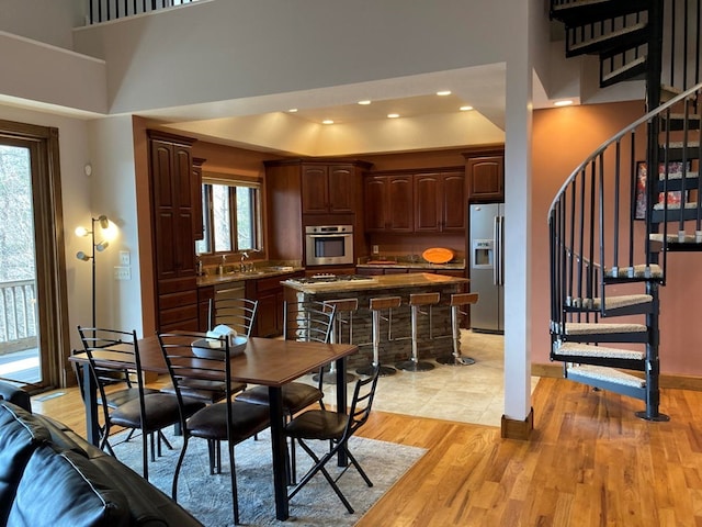 dining space with sink, a raised ceiling, a high ceiling, and light hardwood / wood-style floors