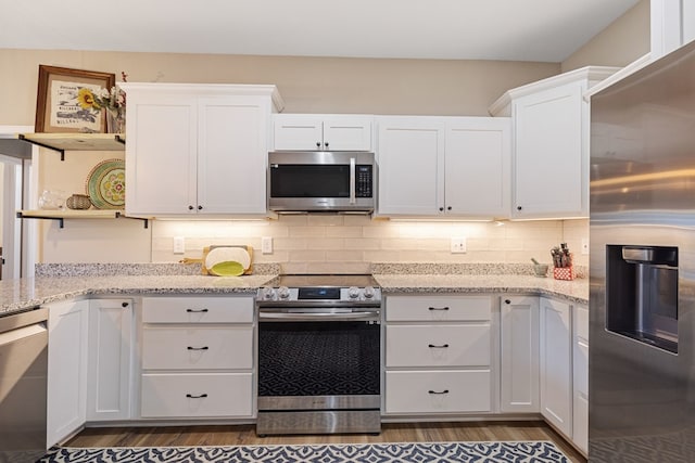 kitchen featuring appliances with stainless steel finishes, open shelves, light stone countertops, and white cabinetry