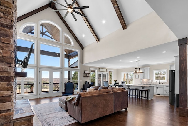 living room with dark wood-type flooring, beam ceiling, ceiling fan with notable chandelier, french doors, and high vaulted ceiling