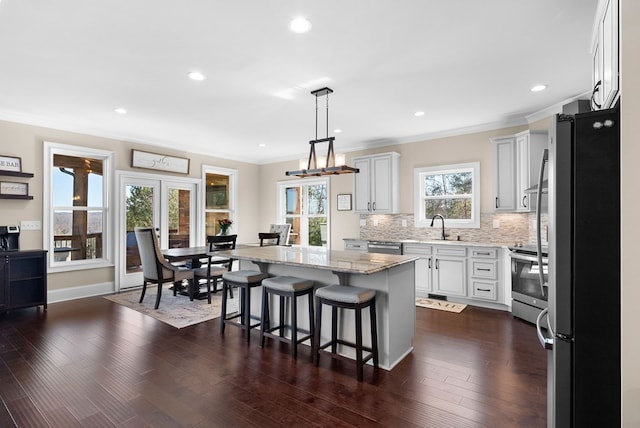 kitchen with dark wood-type flooring, light stone counters, tasteful backsplash, a kitchen island, and appliances with stainless steel finishes