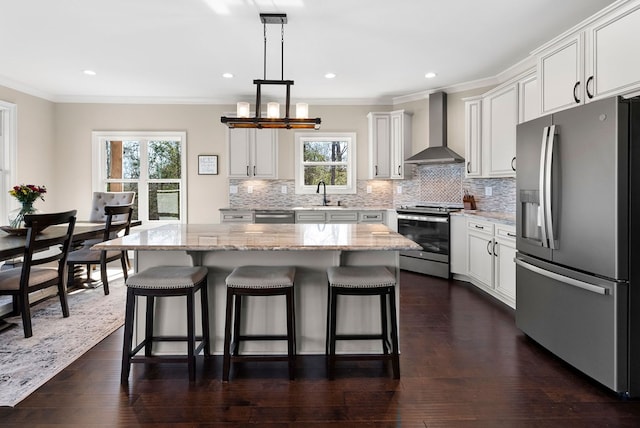 kitchen with a breakfast bar, a sink, appliances with stainless steel finishes, wall chimney exhaust hood, and decorative backsplash