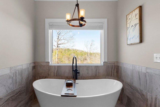 bathroom featuring tile walls, a notable chandelier, wainscoting, and a freestanding bath