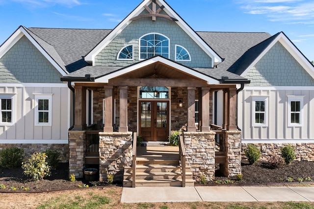 craftsman-style house featuring stone siding, french doors, board and batten siding, and roof with shingles