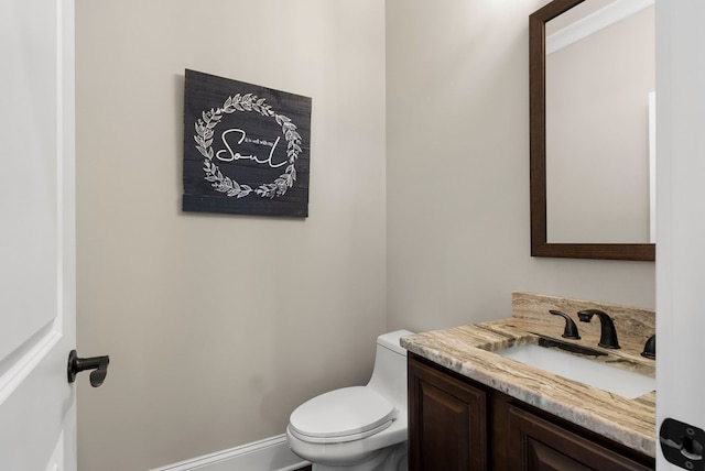 half bathroom featuring baseboards, toilet, and vanity