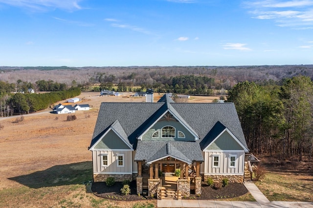 view of front of property with board and batten siding, a porch, roof with shingles, a view of trees, and stone siding