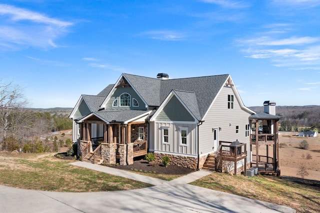 view of front of home with board and batten siding, a porch, a front yard, roof with shingles, and cooling unit