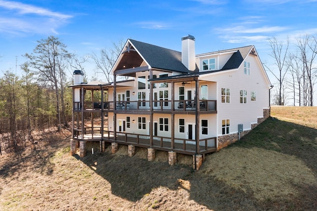 rear view of property featuring a lawn, a chimney, a deck, and a shingled roof