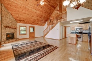 living room with high vaulted ceiling, wood ceiling, light wood-type flooring, and a stone fireplace