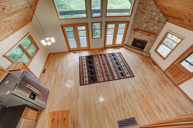 unfurnished living room featuring hardwood / wood-style floors, high vaulted ceiling, a fireplace, french doors, and a chandelier