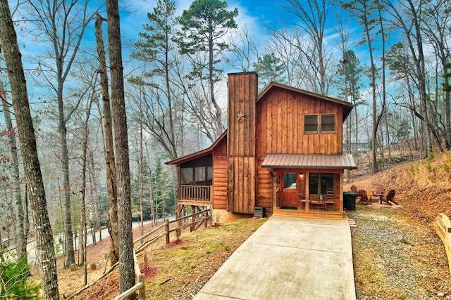 rustic home featuring driveway, covered porch, a chimney, board and batten siding, and metal roof