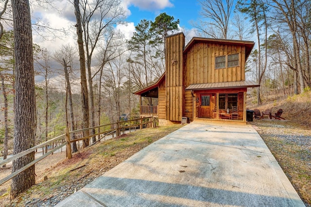 chalet / cabin featuring a porch, a chimney, board and batten siding, and metal roof