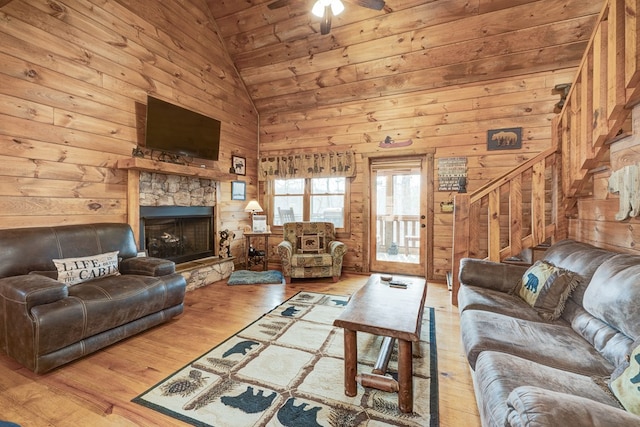 living area with stairway, wood finished floors, high vaulted ceiling, a fireplace, and wood walls